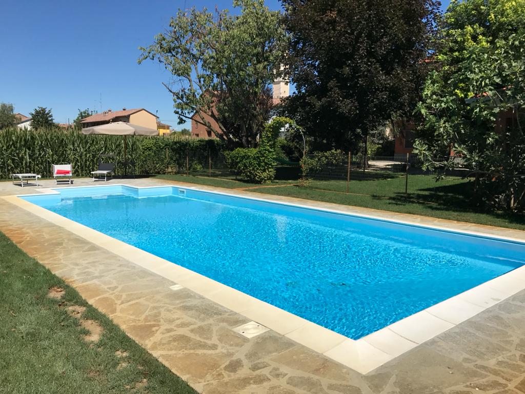 Piscina rettangolare finita, con bordo e pavimentazione in pietra e prato attorno
