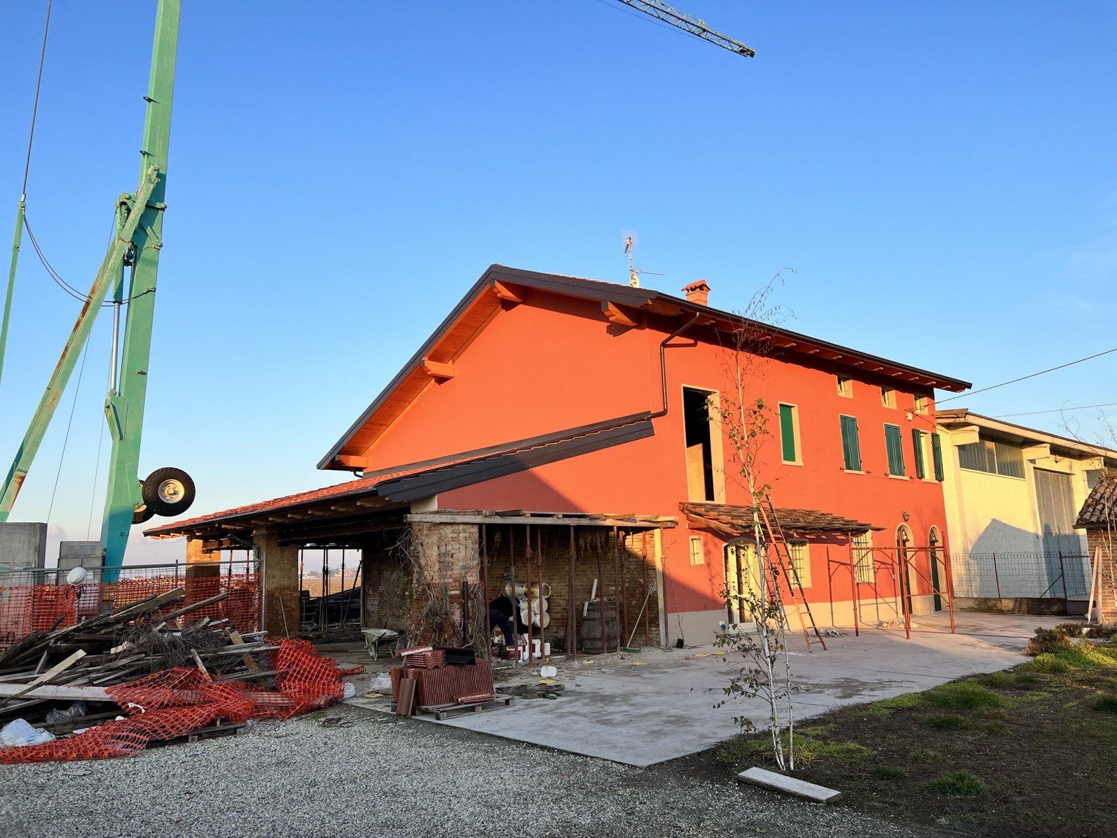 Cascina con intonaco arancio nuovo, serramenti verdi e tetto rifatto con travi in legno a vista; il portico laterale e' ancora in lavorazione e l'autogru e' in opera