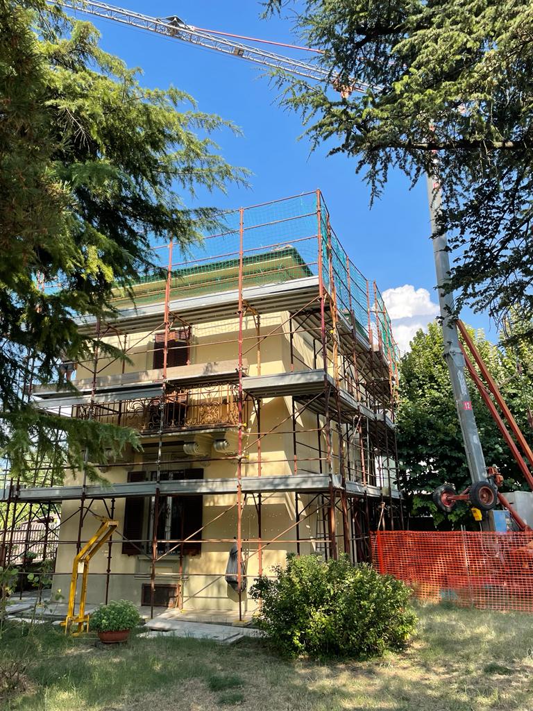 Villa a tre piani con ponteggio su tutti i lati, reti di protezione sul tetto e autogru a fianco