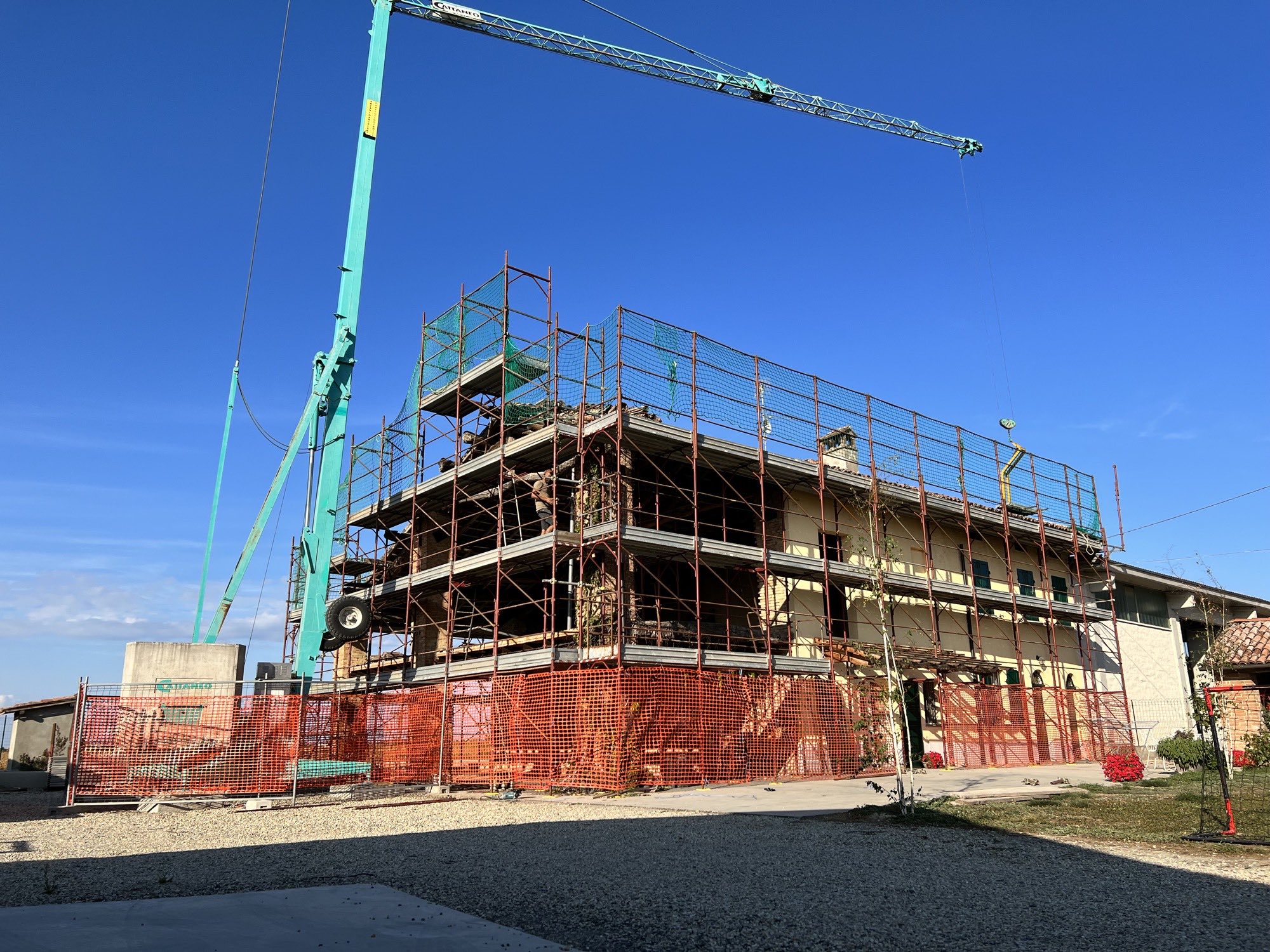 La cascina prima dell'intervento: ponteggio e reti di cantiere su tutti i lati, gru in opera, struttura a vista e intonaco vecchio ancora sull'ala destra